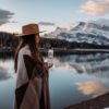 woman in brown coat wearing brown hat standing near lake during daytime