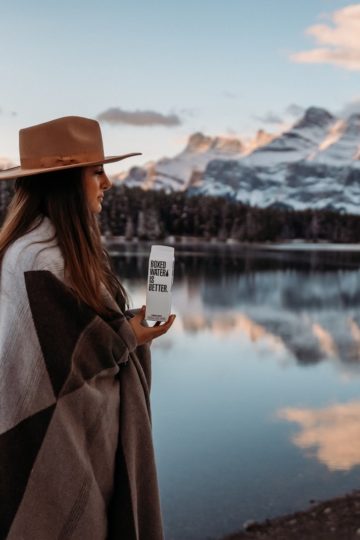 woman in brown coat wearing brown hat standing near lake during daytime